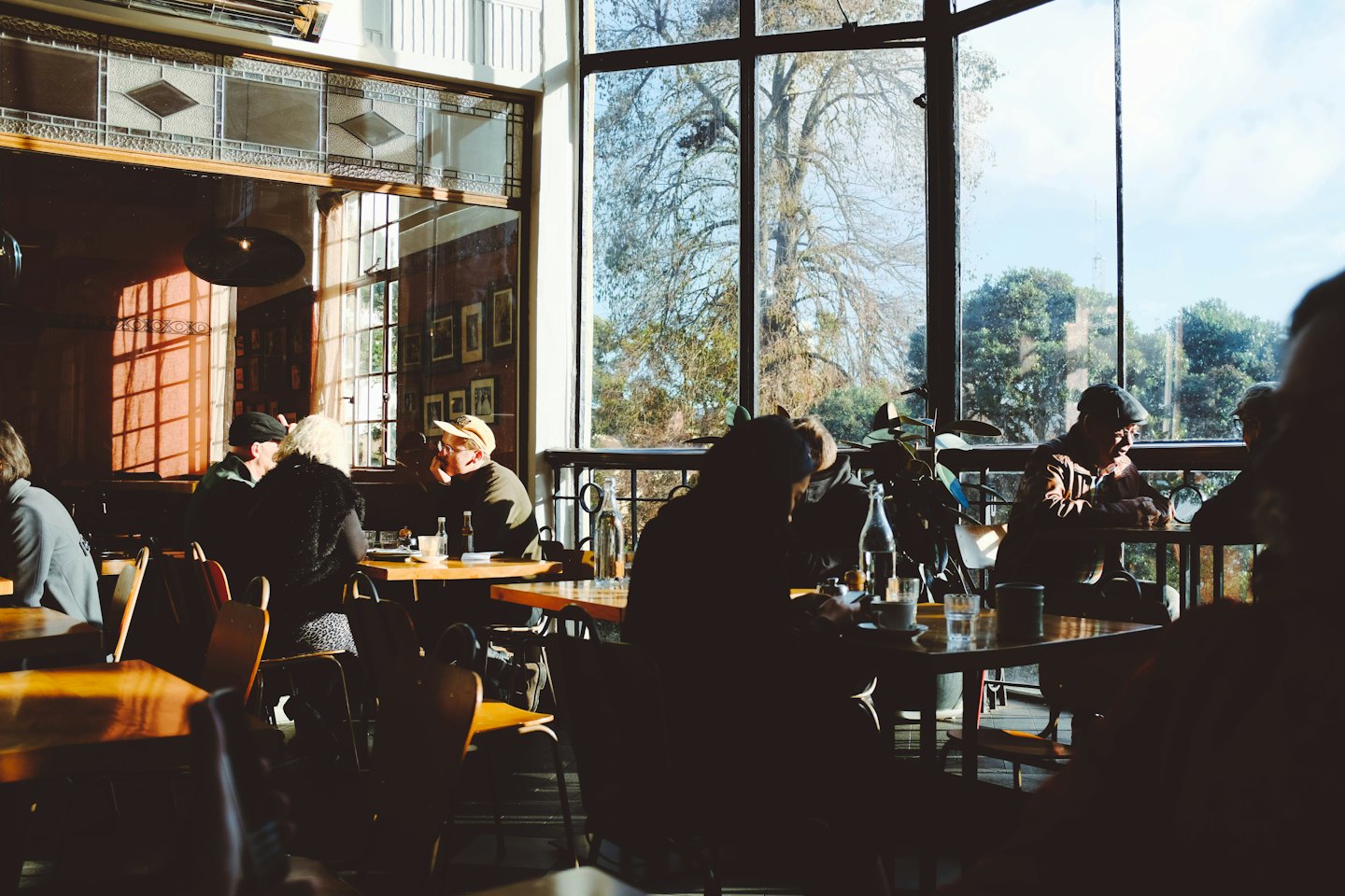 Patrons sit at tables inside a bright, sunlit cafe.
