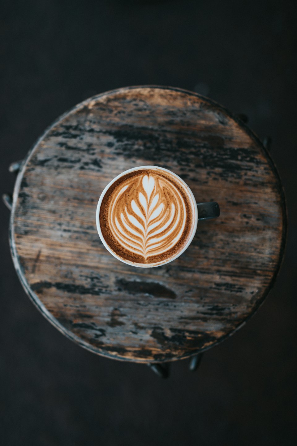 White ceramic mug with leaf latte art on a wooden table.