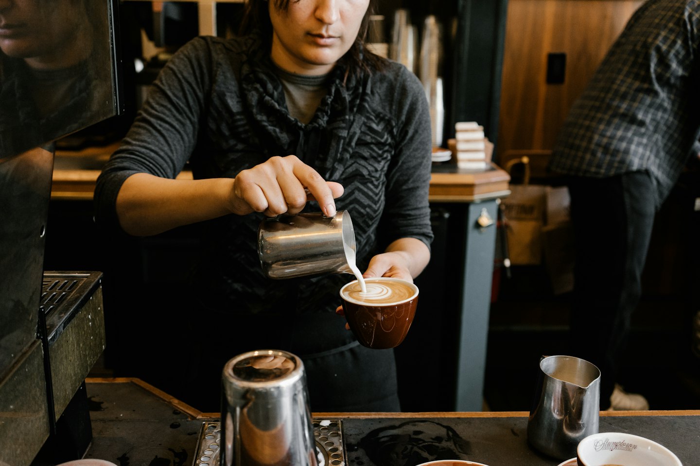 Barista pours steamed milk into coffee cup to make latte art.